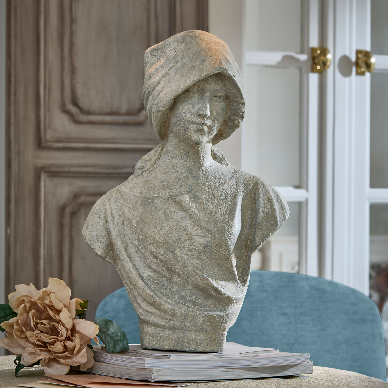 Busto Mireline Busto de mujer en piedra gris sobre libros con flor decorativa al lado en interior elegante