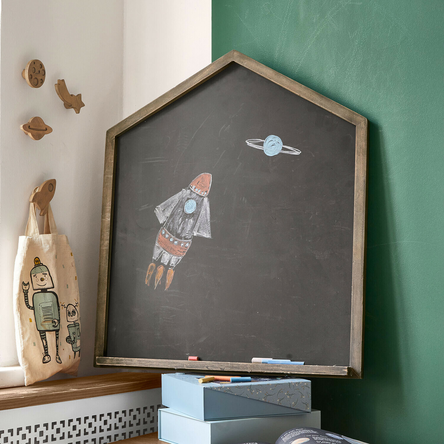 Pizarra en forma de casa con marco de madera y dibujo de cohete y planeta en habitación infantil
