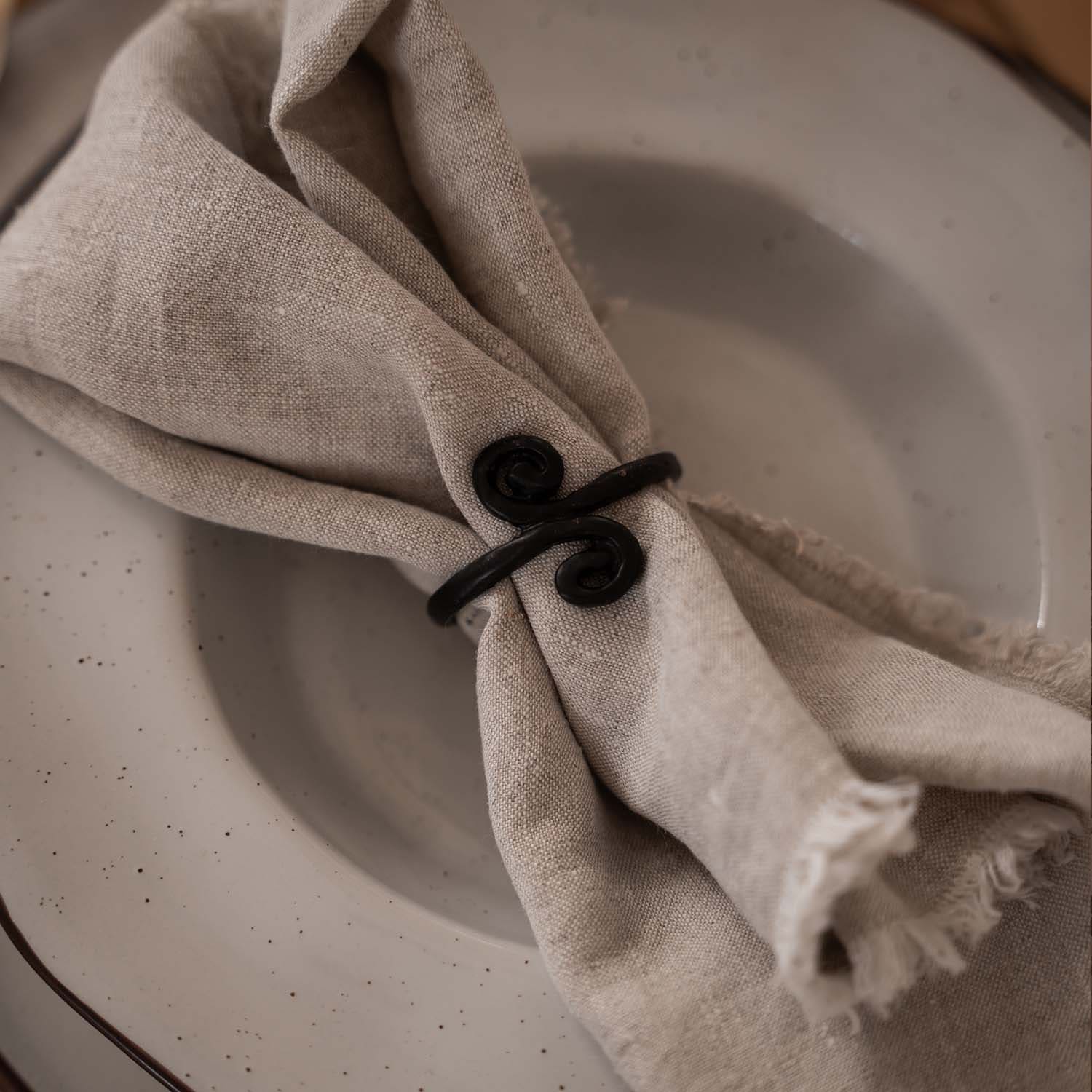Servilleta de lino beige con anillo metálico negro sobre plato claro