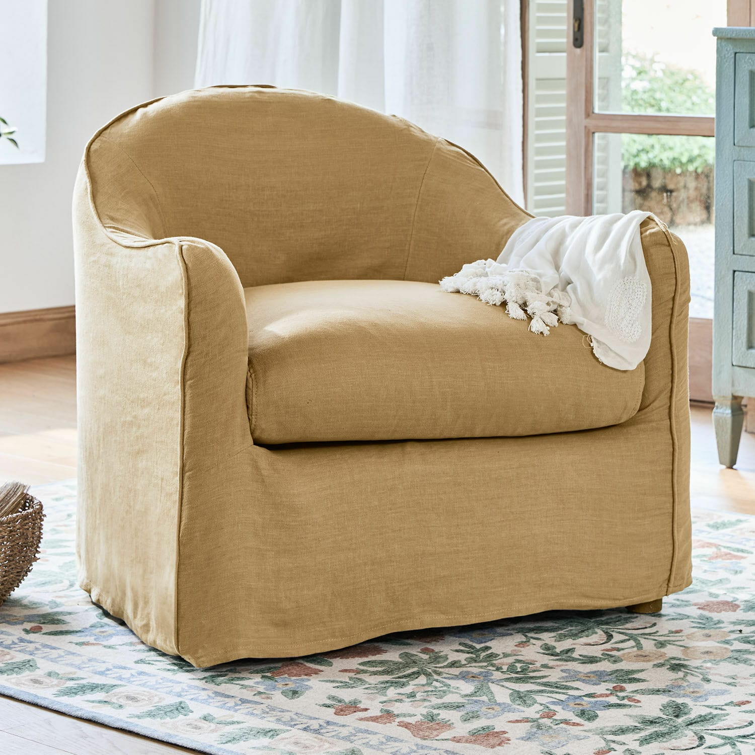 Sillón beige de lino con cojín suave sobre alfombra floral para sala de estar