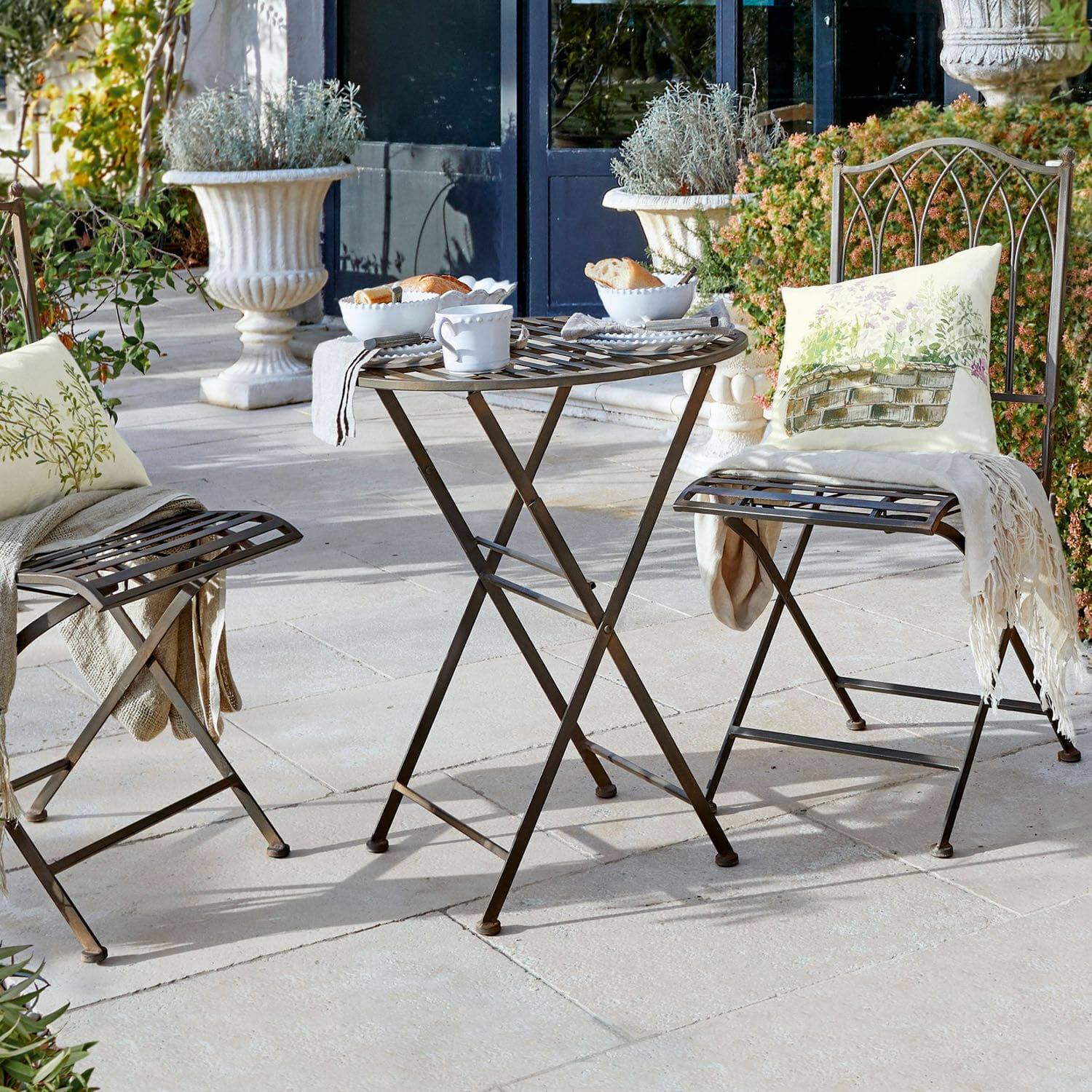 Mesa Brignoles Mesa y sillas plegables de metal marrón en terraza con cojines decorativos y vajilla blanca