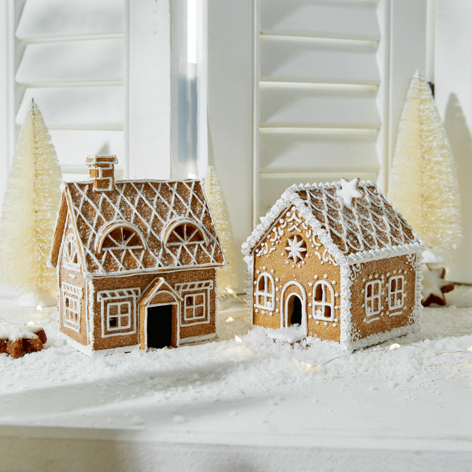 Dos casas de jengibre decoradas con glaseado blanco sobre mesa navideña con decoración invernal