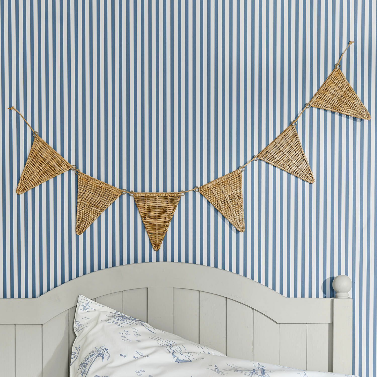 Guirnalda de banderines Anglemont Guirnalda decorativa de mimbre en forma de triángulos sobre pared a rayas azul y blanca en dormitorio