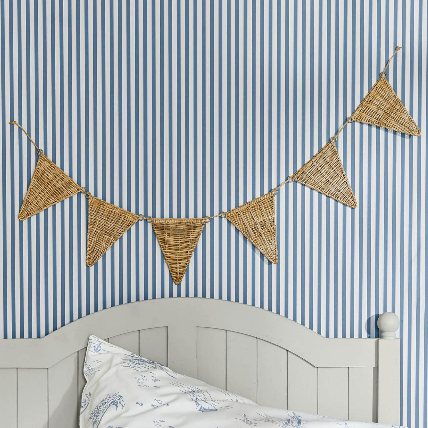 Guirnalda de banderines Anglemont Guirnalda decorativa de mimbre en forma de triángulos sobre pared a rayas azul y blanca en dormitorio