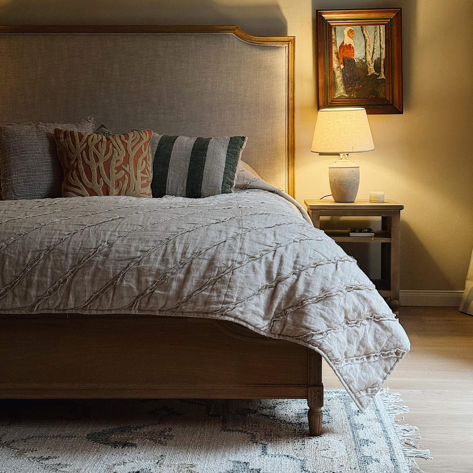Dormitorio acogedor con cama de madera, colcha beige y lámpara sobre mesita de noche de madera