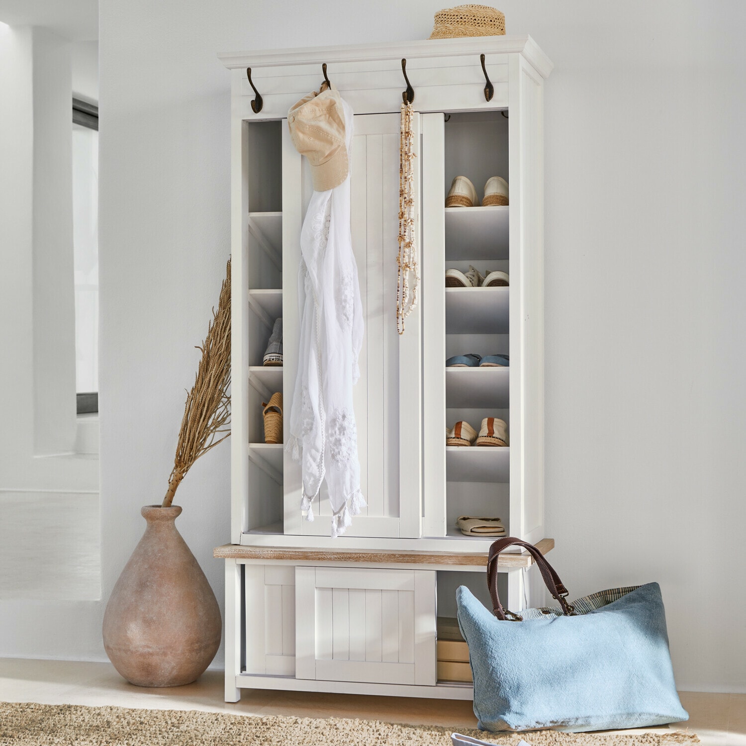 Armario para zapatos de madera blanca con ganchos y estantes, bolso azul y sombrero de paja