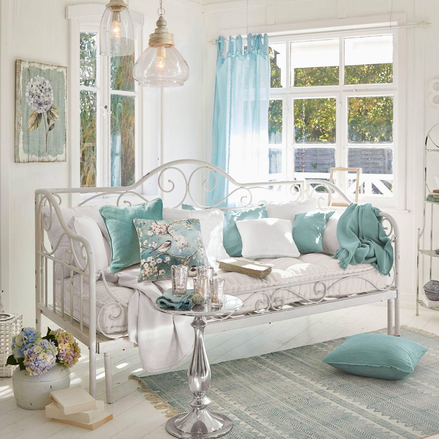 Sofá cama Maditha Sofá metálico blanco con cojines suaves y detalles turquesa en sala luminosa con ventana grande