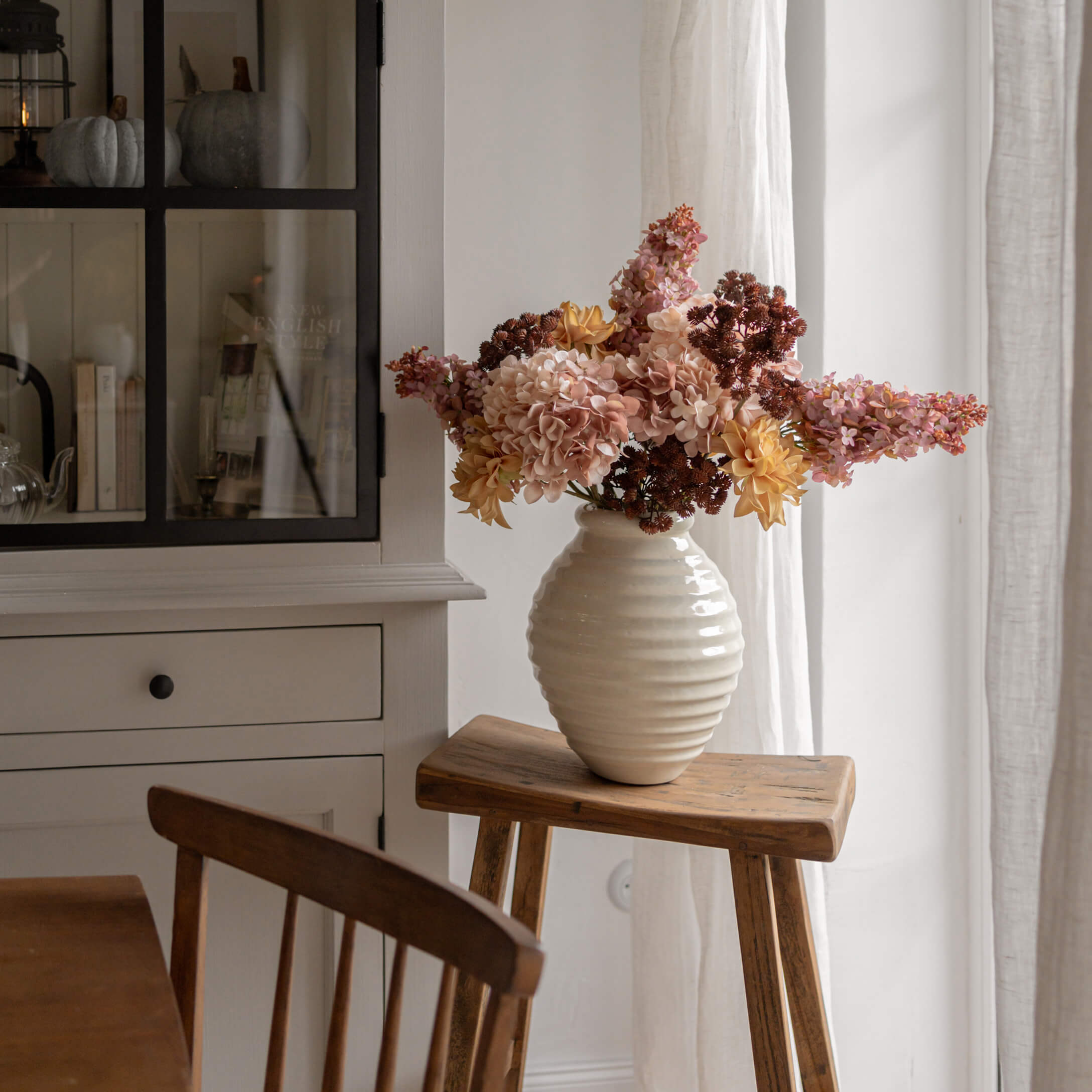 Jarrón de alabastro blanco con flores amarillas y rosas sobre taburete de madera en interior luminoso