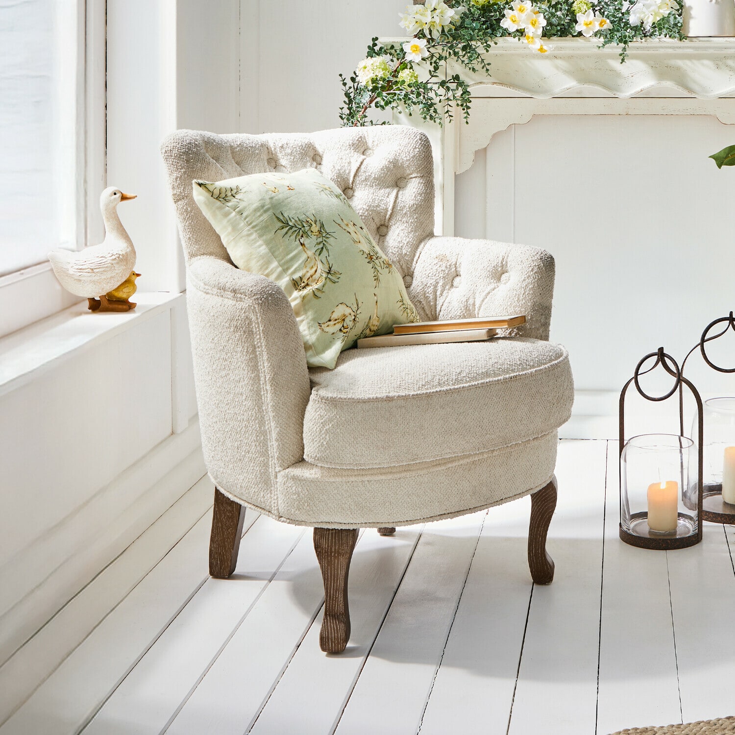 Sillón Calgary Sillón beige de tela suave con patas de madera y cojín verde con flores en interior luminoso