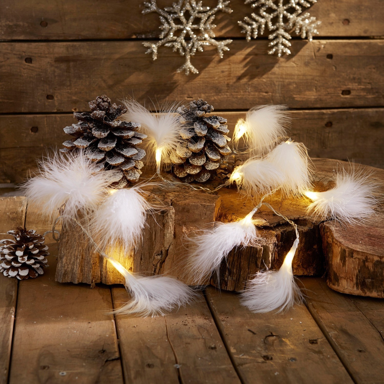 Guirnalda luminosa con plumas blancas sobre fondo de madera con piñas y decoración invernal