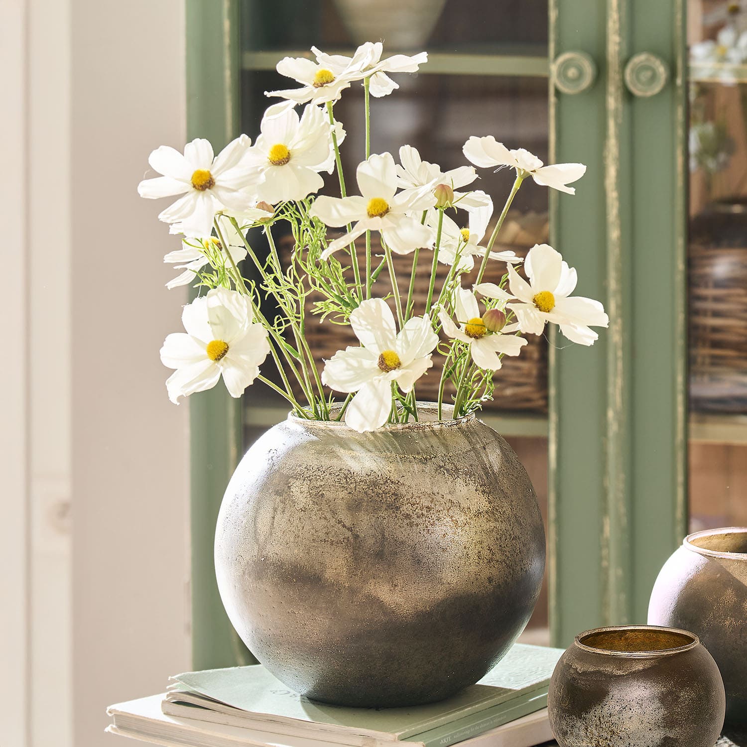 Jarrón redondo de metal plateado con flores blancas sobre libros, decoración interior elegante