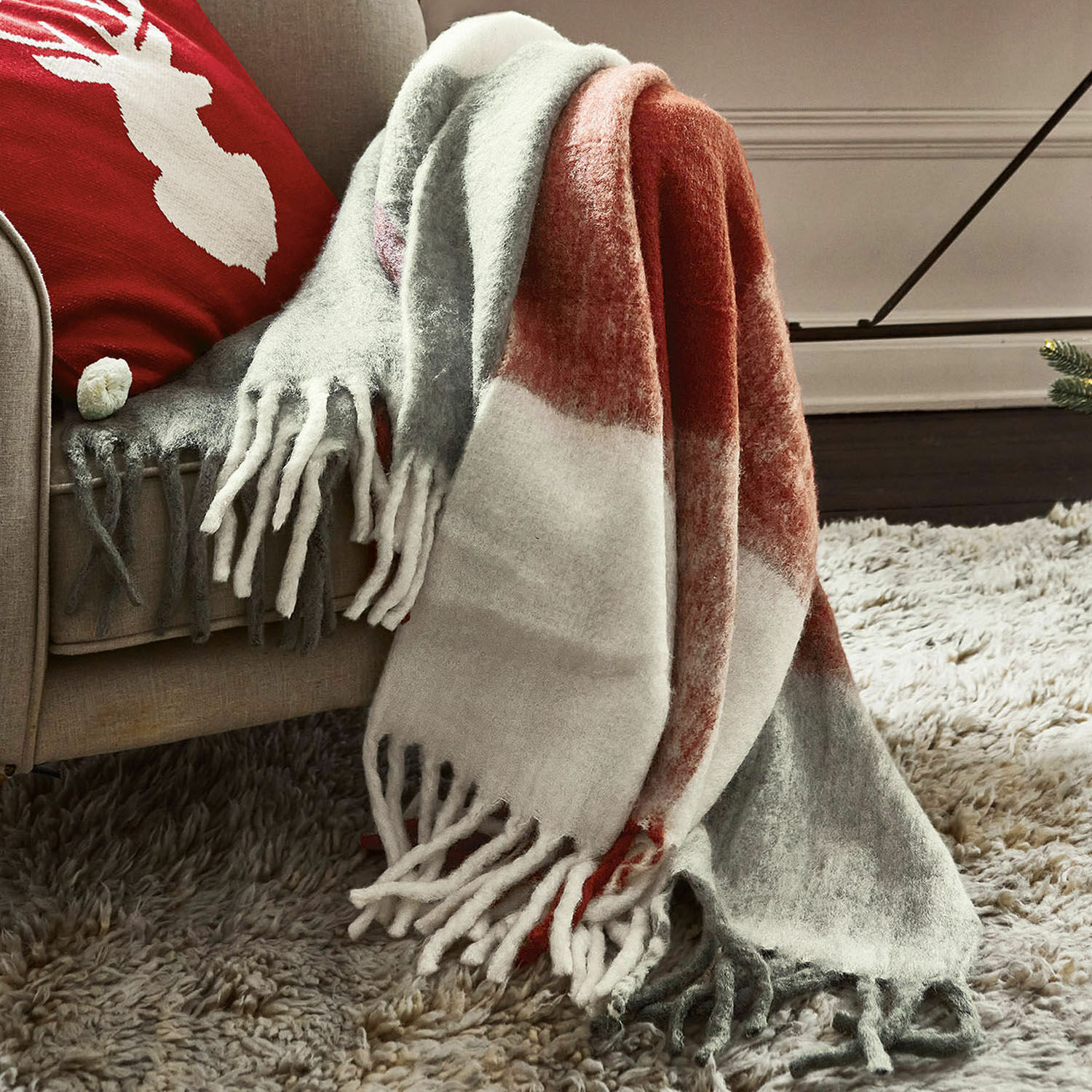 Plaid McGreg Manta suave con flecos en gris, blanco y rojo sobre sofá beige, decoración acogedora para salón