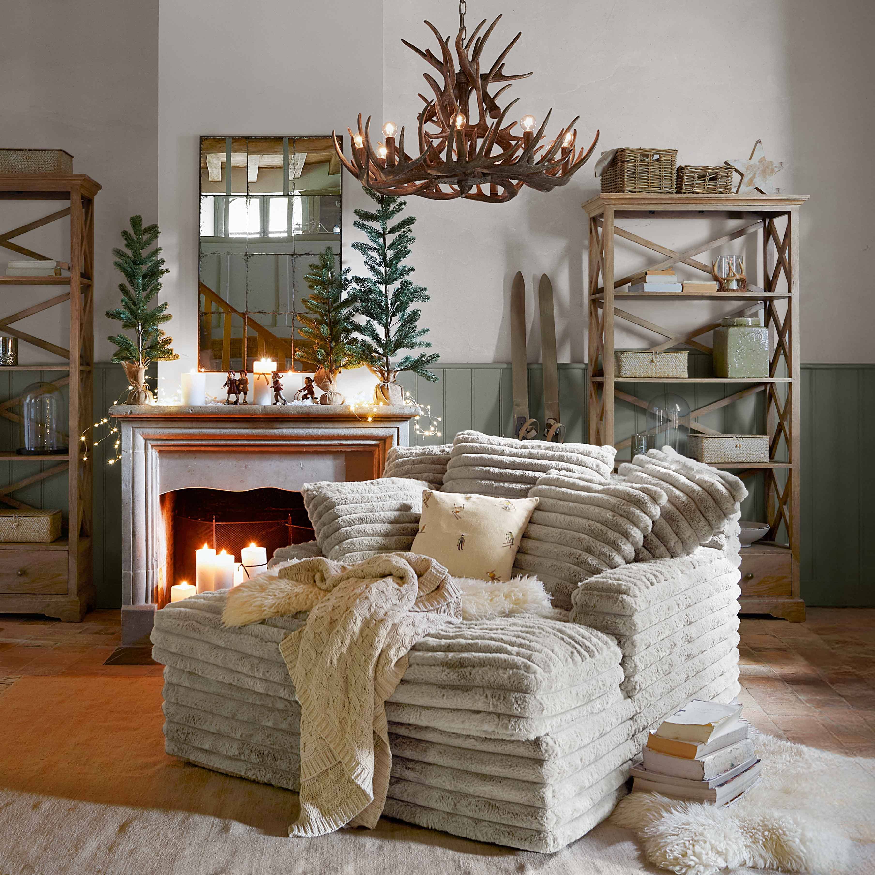 Sillón beige de tela suave con manta y cojín en salón rústico con chimenea y decoración acogedora