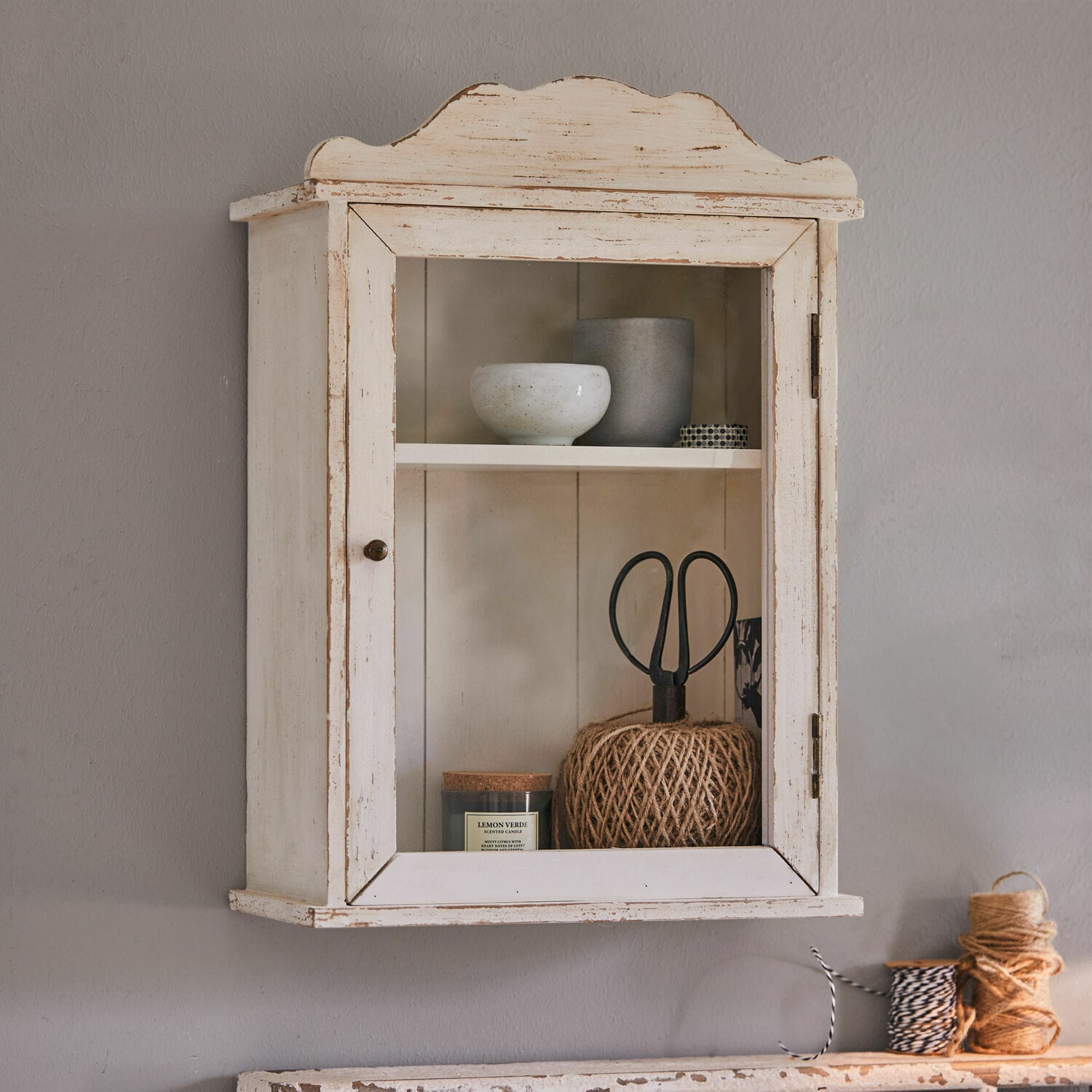 Armario de pared Sandrine Armario de pared de madera blanca envejecida con puerta de cristal y objetos decorativos en su interior