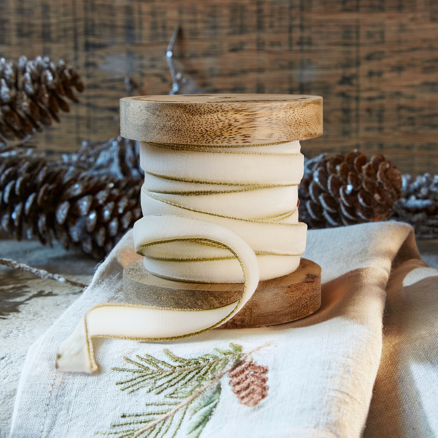 Cinta de terciopelo Sorima Carrete de madera natural con cinta crema y borde verde sobre tela de lino con bordado de piña