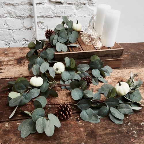 Guirnalda decorativa con hojas verdes de eucalipto, mini calabazas blancas y piñas sobre mesa de madera