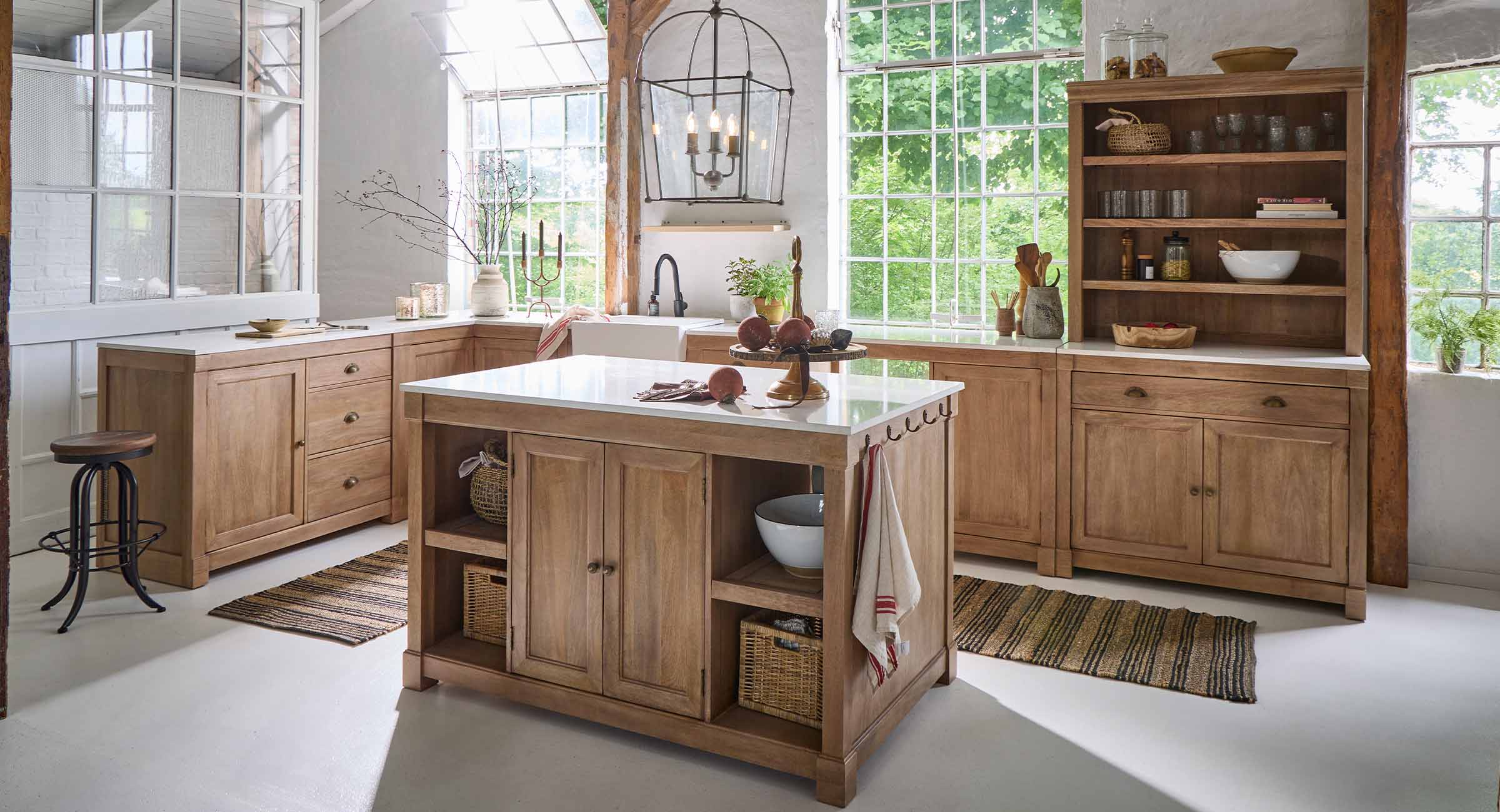 Cocina con isla y muebles de roble natural, encimeras blancas y grandes ventanas luminosas