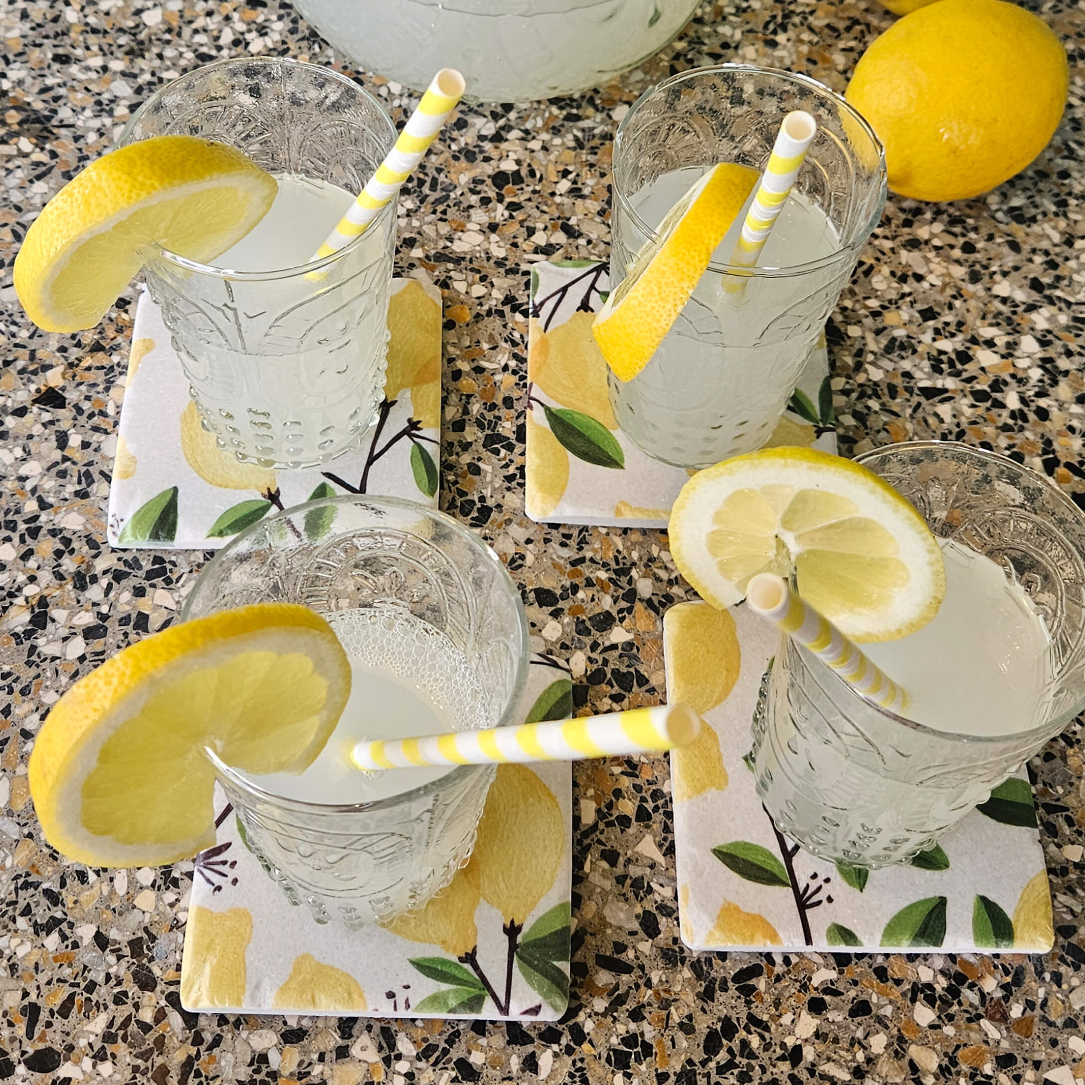 Vasos con limonada y rodajas de limón sobre posavasos de cerámica con diseño de limón en encimera de piedra
