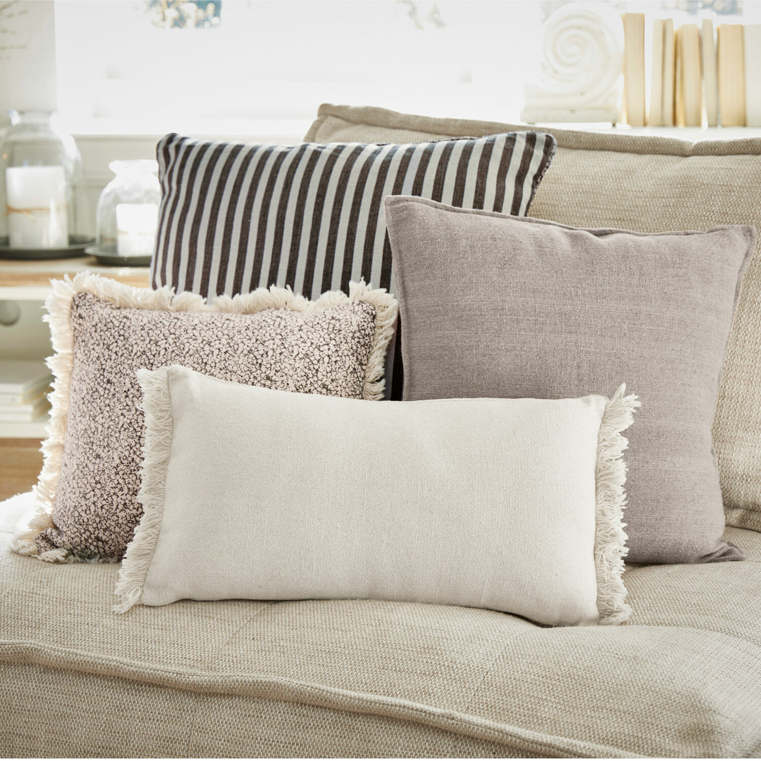 Set de 4 cojines Valenciennes Conjunto de cuatro cojines decorativos en tonos neutros sobre un sofá beige para sala