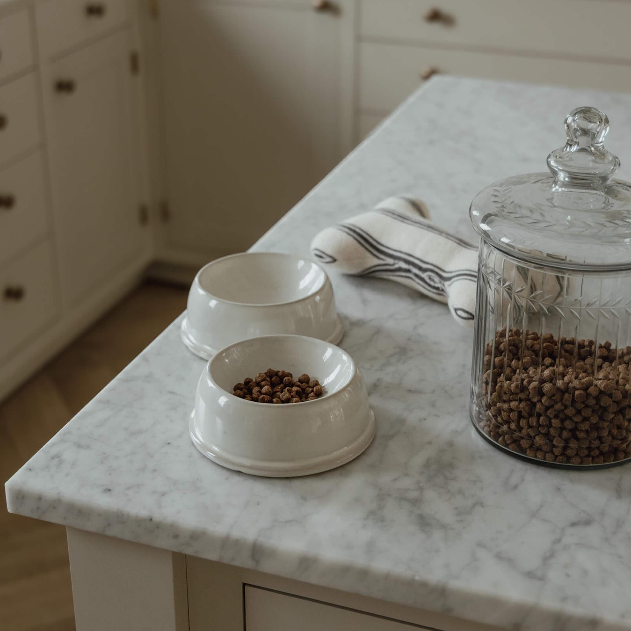 Cuencos de cerámica blanca con pienso seco y tarro de cristal sobre encimera de mármol