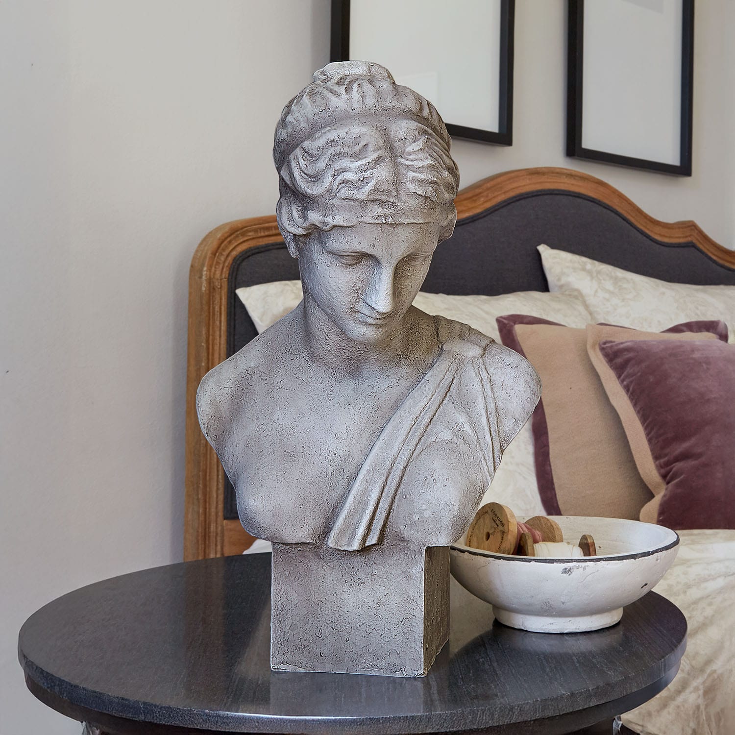 Busto de piedra gris sobre mesa negra en dormitorio elegante con cojines decorativos