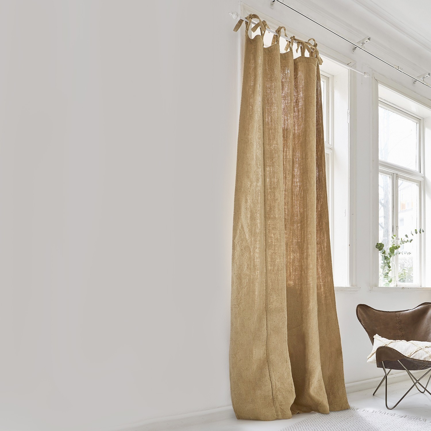 Cortina Uma Cortina beige de lino natural en habitación luminosa con ventana grande y sillón marrón