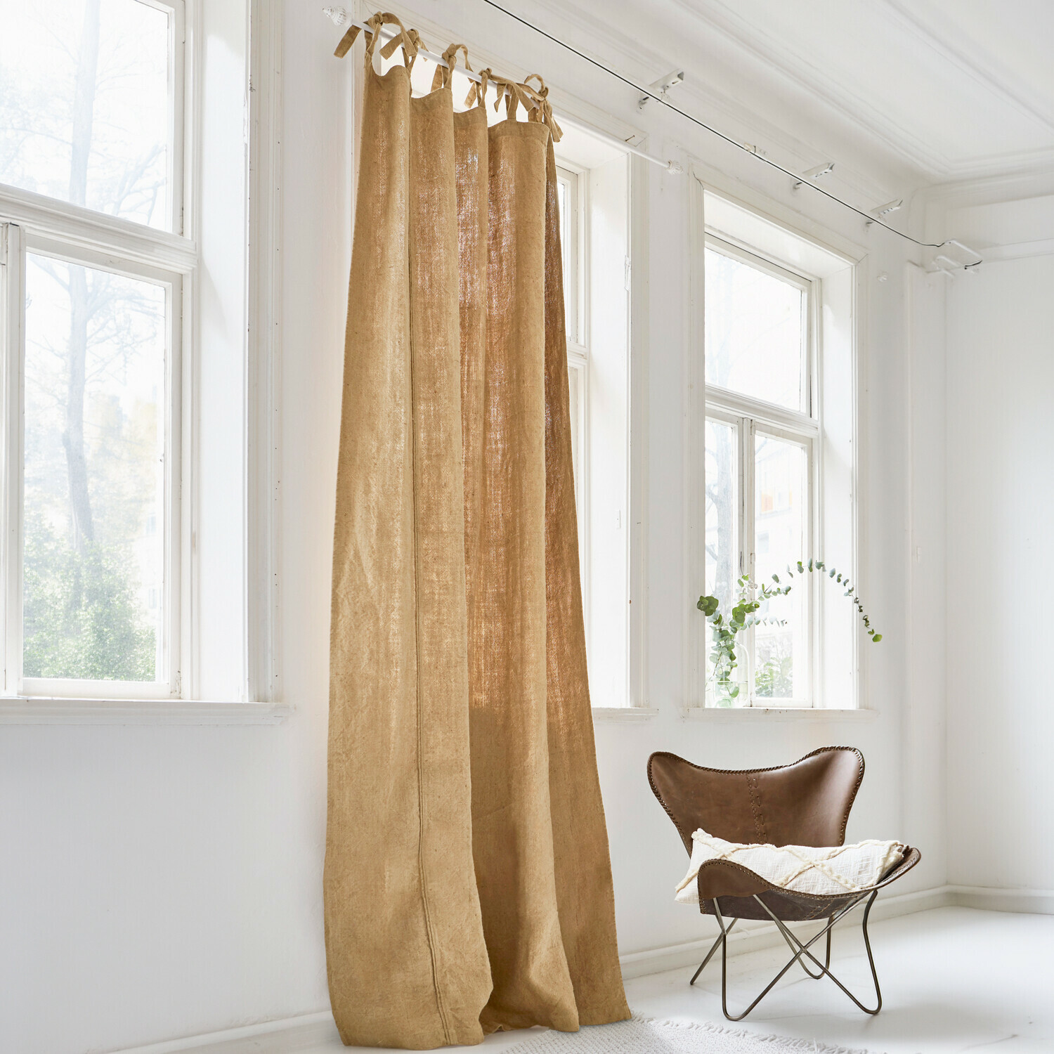 Cortina beige de lino natural en habitación luminosa con ventana grande y sillón marrón