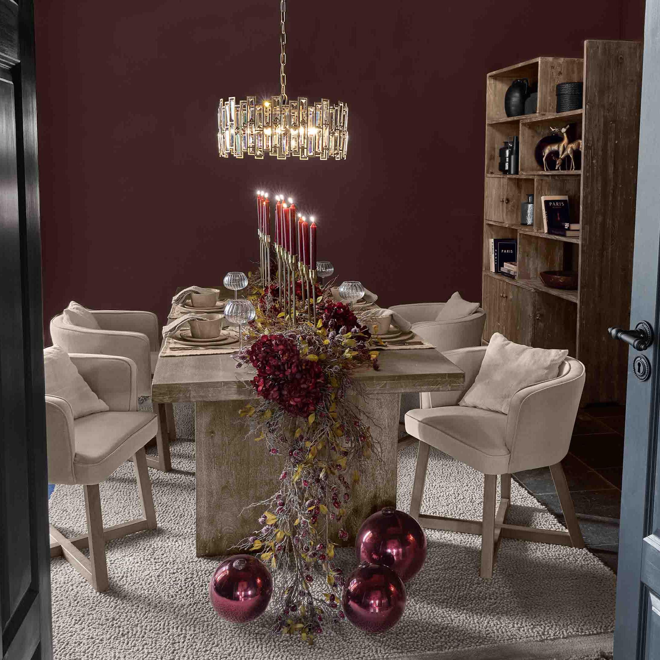 Comedor con mesa de madera, sillas beige y decoración con velas rojas y bolas navideñas brillantes