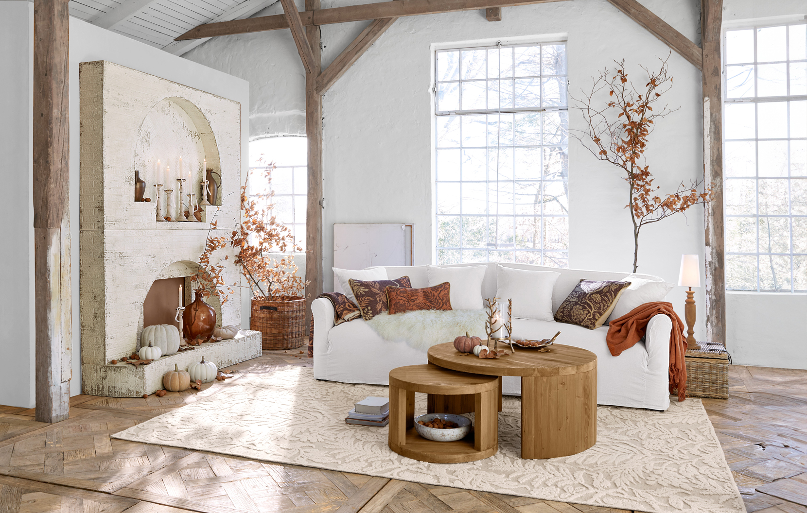 Acogedor salón rústico con sofá blanco, mesas de madera redondas y decoración otoñal en tonos marrones cálidos