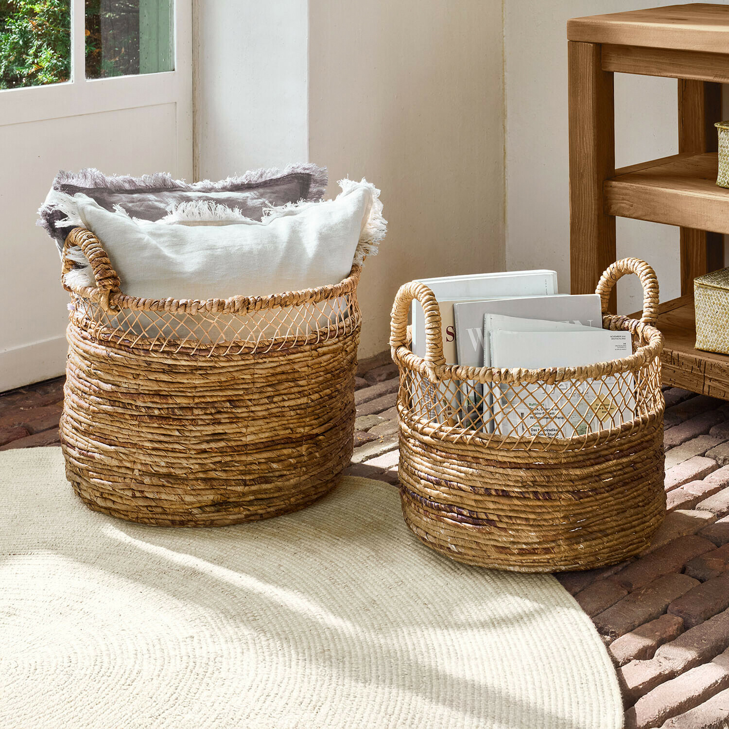 Set de 2 cestas Dorelin Dos cestas de mimbre natural con asas, llenas de cojines y libros para almacenamiento decorativo