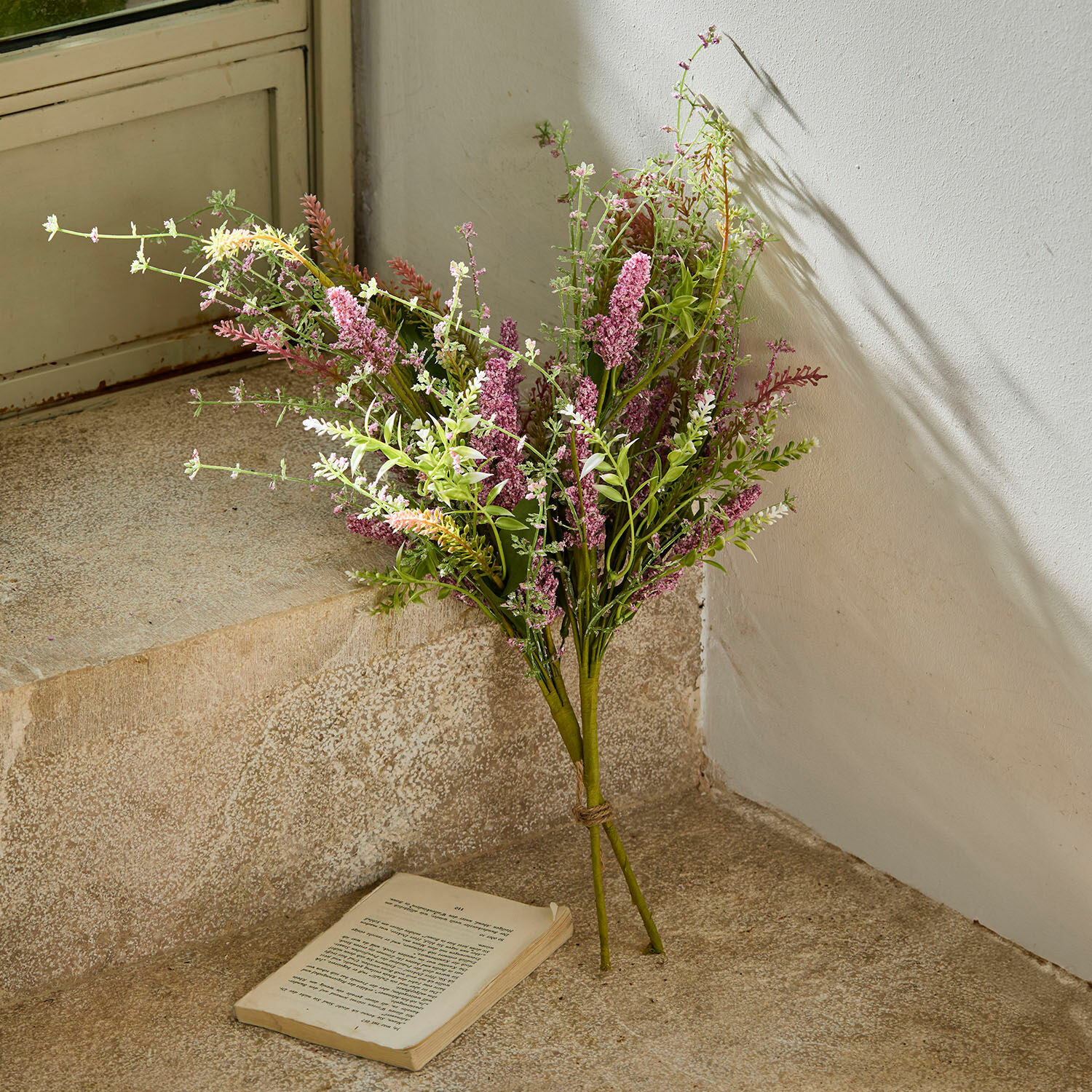 Set de 2 ramos de flores decorativos Oiselette Ramo de flores artificiales en tonos rosas y verdes sobre suelo de piedra con libro abierto