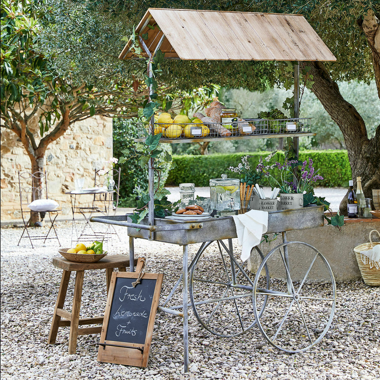 Mesa de jardinería Granby Carrito metálico con techo de madera, frutas frescas y limonada en un jardín soleado
