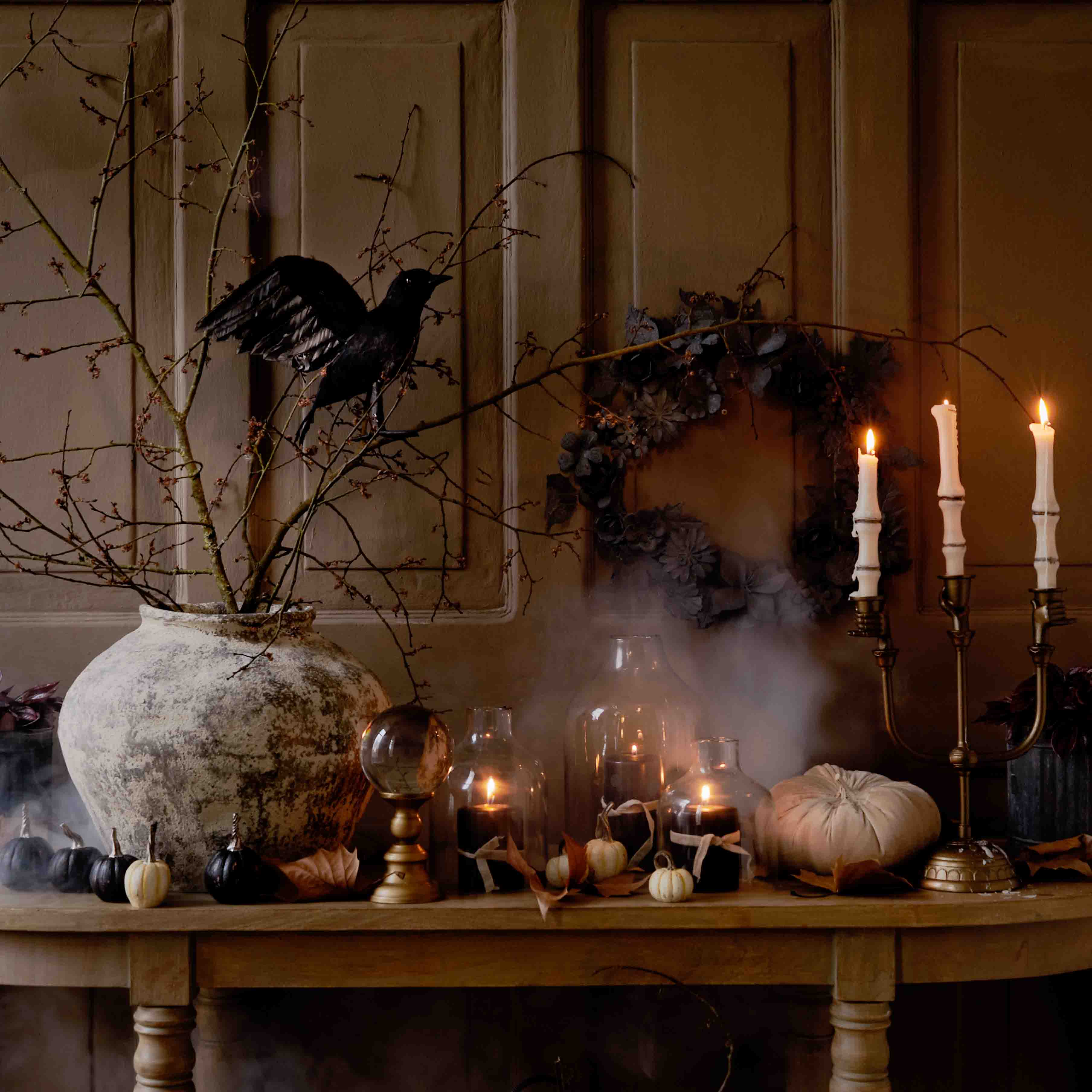 Decoración otoñal de mesa con gran jarrón de cerámica, velas encendidas y pájaro negro en rama