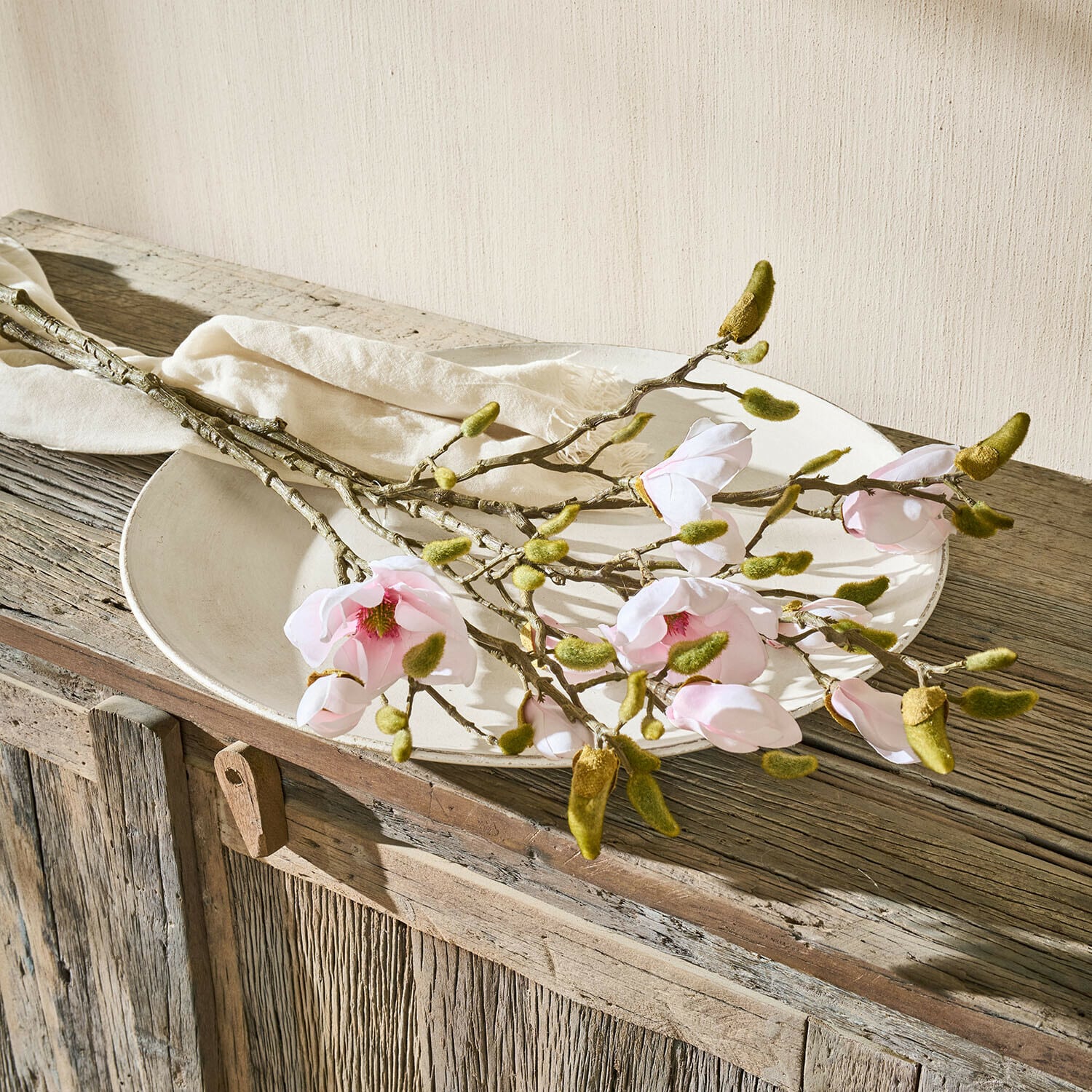 Set de 2 flores decorativas Aurélines Ramas de magnolia con flores rosas y brotes verdes sobre plato blanco en mesa de madera rústica