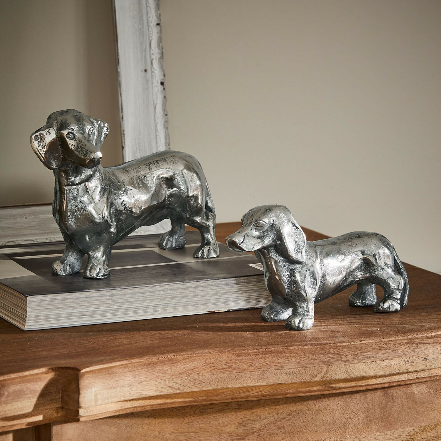 Dos figuras decorativas de teckel de metal plateado sobre mesa de madera, adorno para interiores