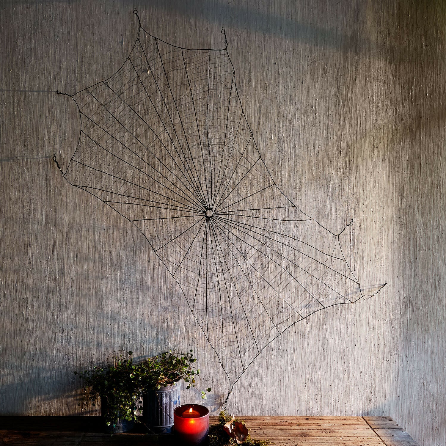 Telaraña decorativa Vexilnor Decoración de pared con telaraña metálica negra, vela roja y planta sobre mesa de madera