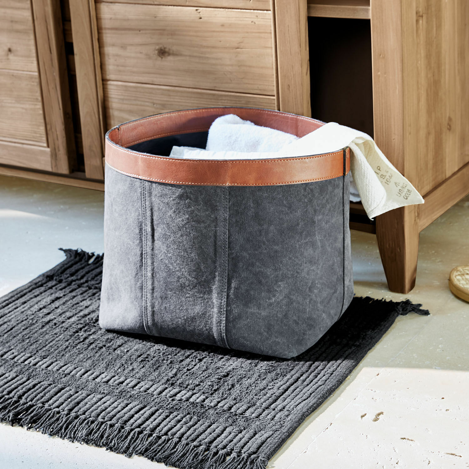 Cesta Chansonet Cesta gris de tela con borde de cuero marrón sobre alfombra negra para guardar textiles