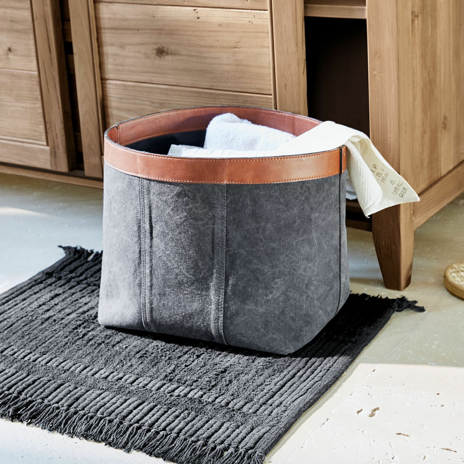 Cesta Chansonet Cesta gris de tela con borde de cuero marrón sobre alfombra negra para guardar textiles