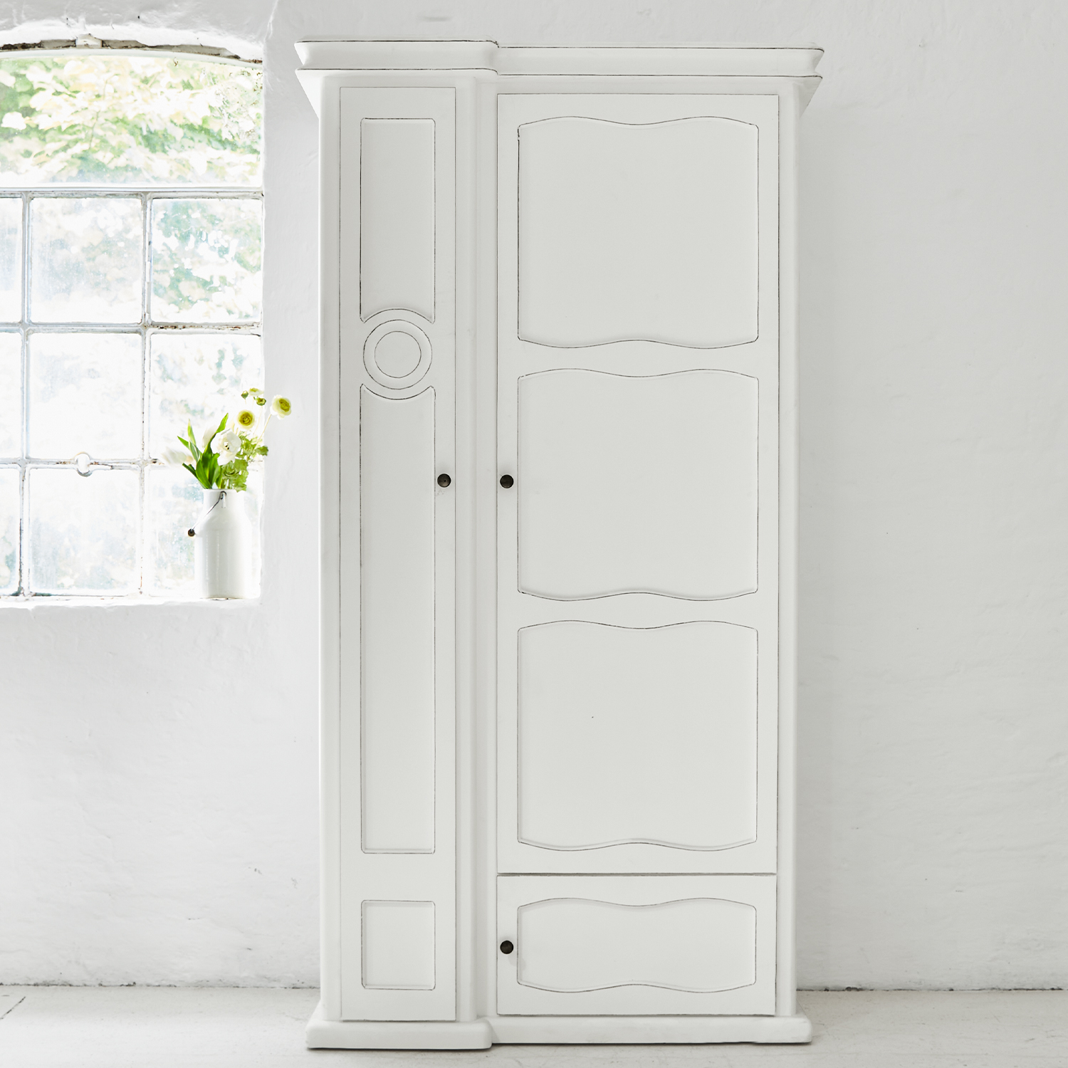 Armario de madera blanco con paneles decorativos y tiradores metálicos en habitación luminosa