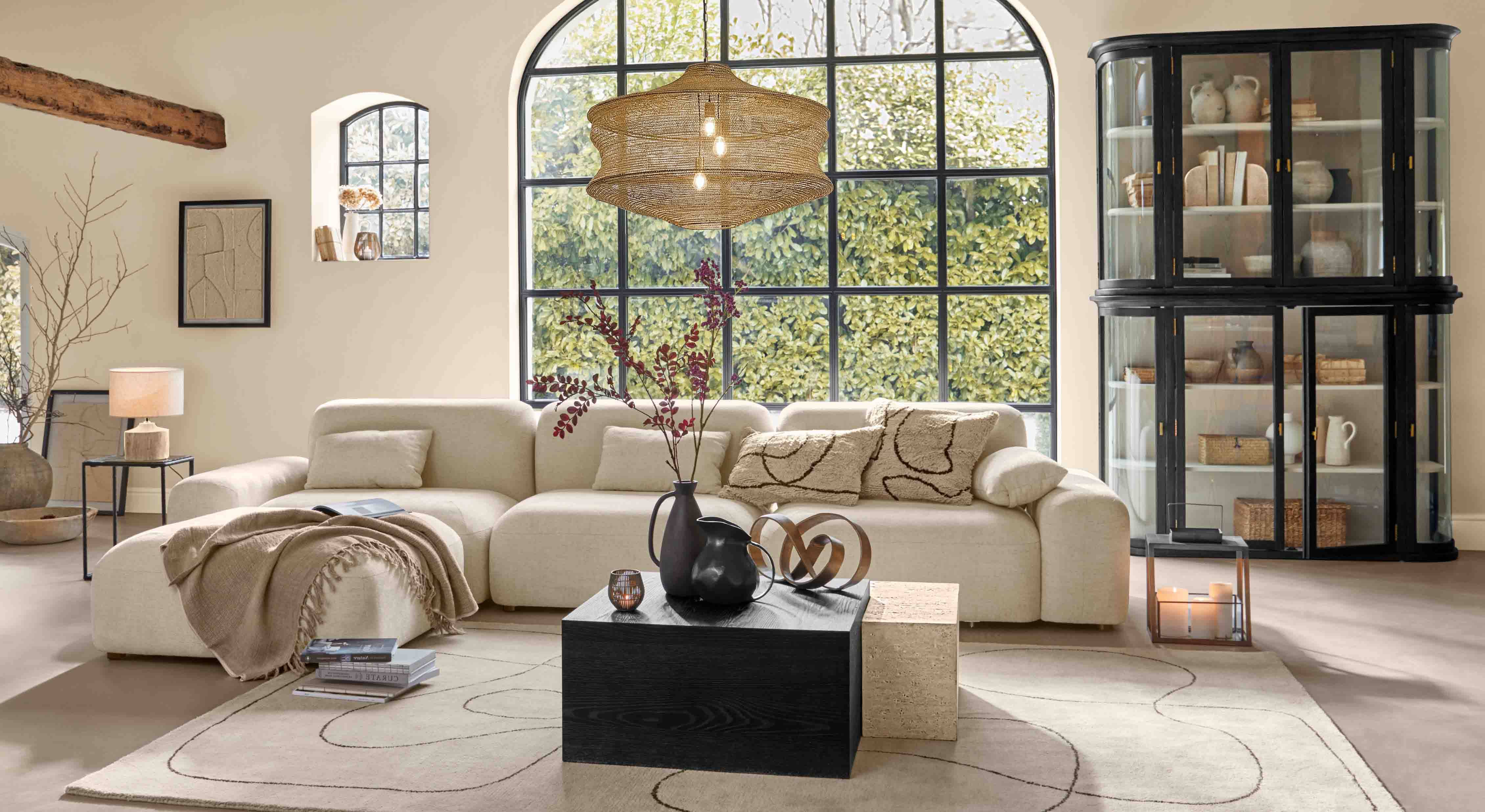 Salón acogedor con sofá beige, mueble negro y ventana grande, iluminación moderna y decoración