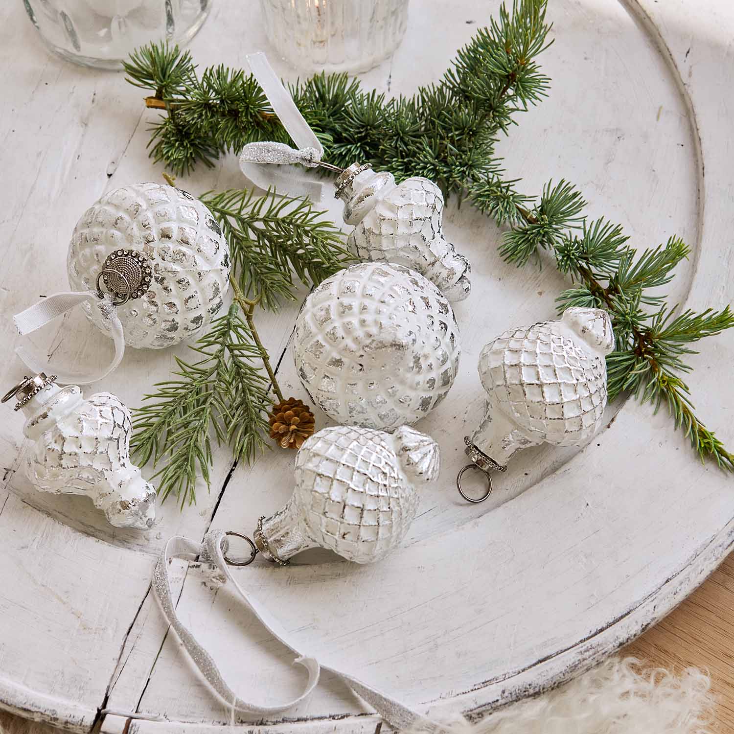 Adornos navideños blancos con textura de rejilla sobre bandeja de madera con ramas de abeto, decoración festiva