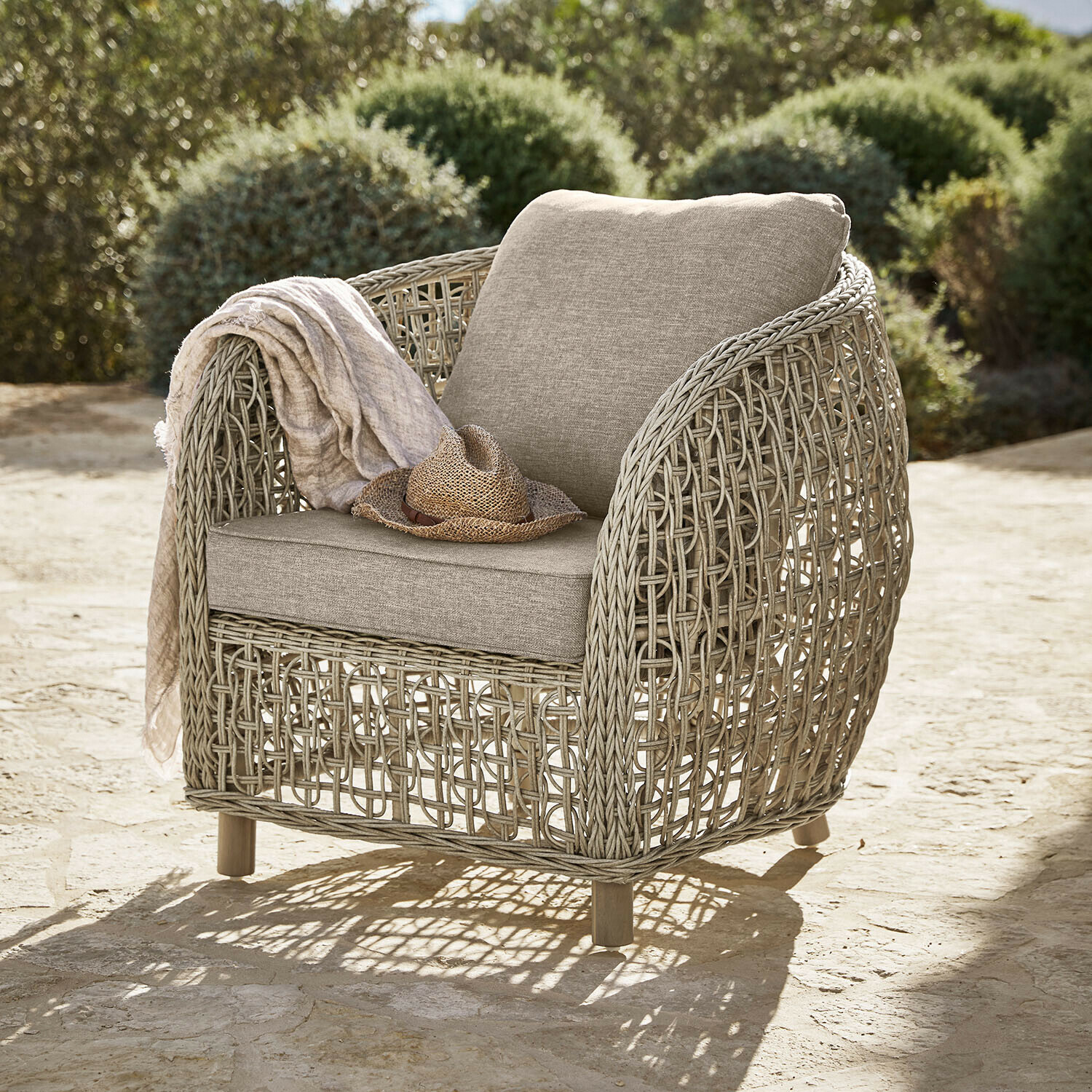 Sillón Ventiglio Sillón de jardín de mimbre beige con cojines beige claro, sombrero y manta sobre el respaldo