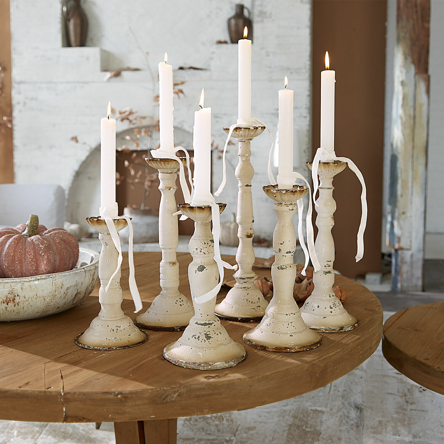 Conjunto de siete candelabros metálicos crema con velas blancas sobre mesa de madera, decoración interior