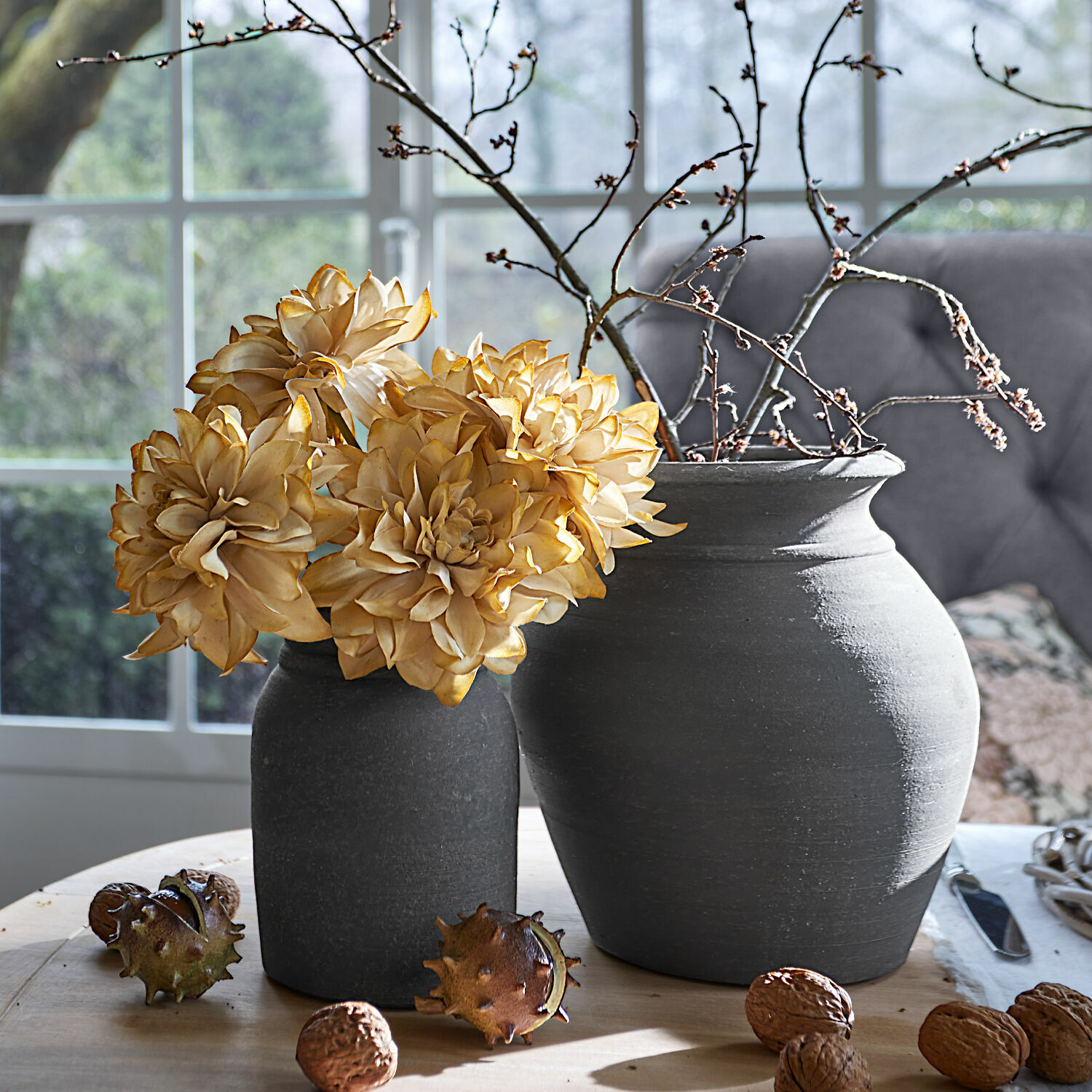 Set de 2 jarrones Molduc Dos jarrones de cerámica gris con flores secas y ramas sobre mesa de madera con nueces