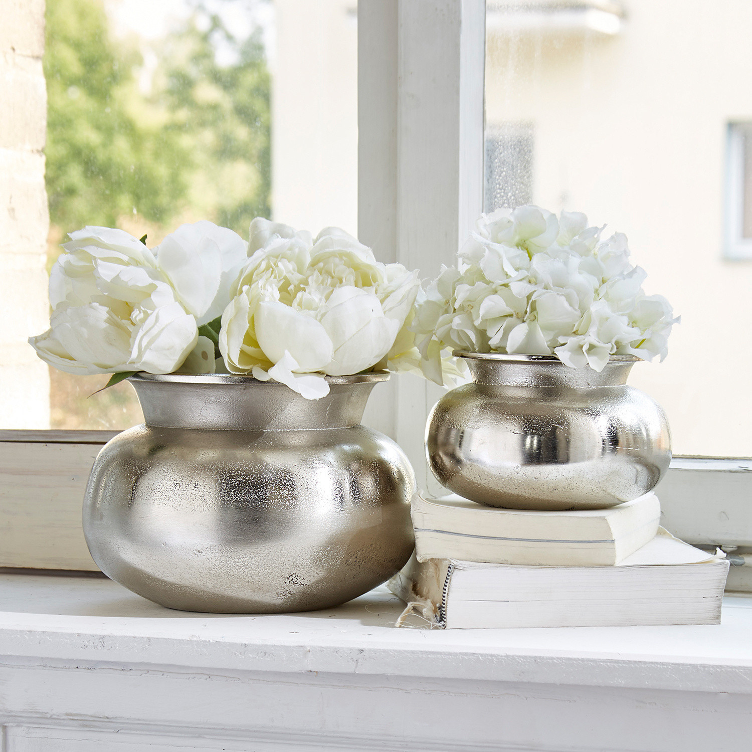 Set de 2 jarrones Clément Dos jarrones metálicos plateados con flores blancas en el alféizar, decoración vintage para interiores