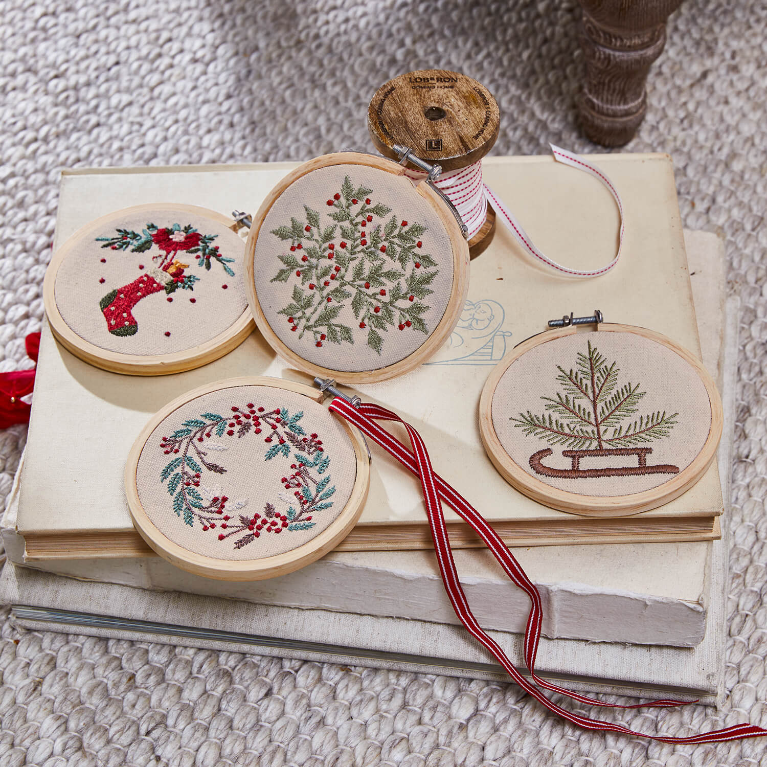 Conjunto de cuatro adornos navideños bordados con motivos vegetales y detalles rojos sobre fondo beige