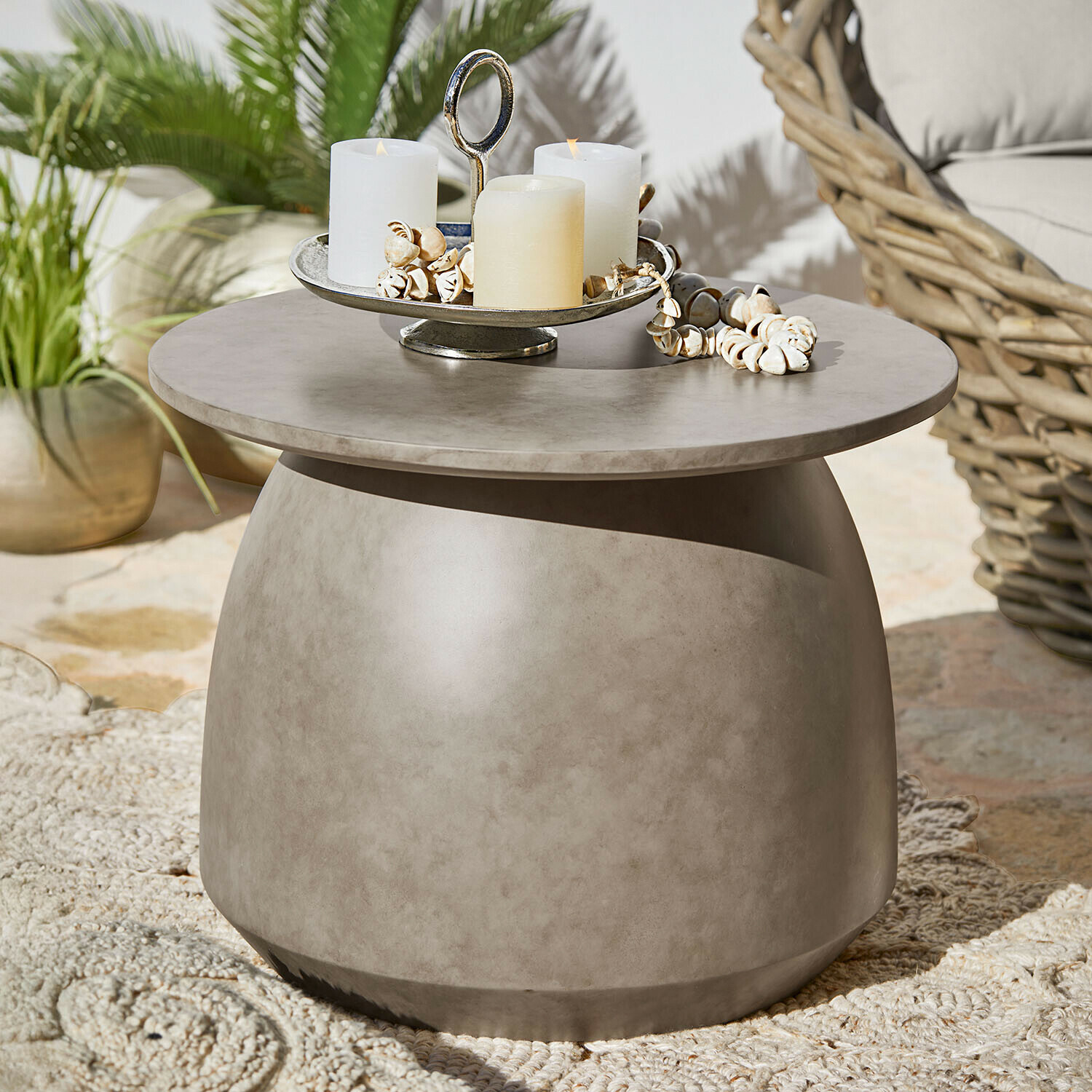 Mesa auxiliar Thyraen Mesa auxiliar redonda de hormigón gris con velas y decoración de conchas en terraza