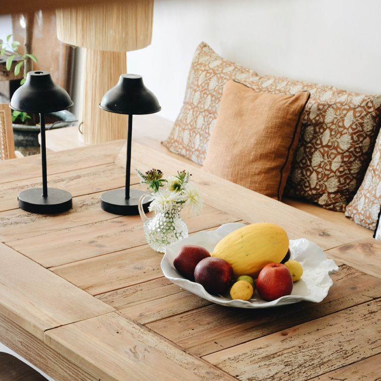 Mesa de madera con cuenco blanco decorativo con frutas y dos lámparas negras en un interior acogedor