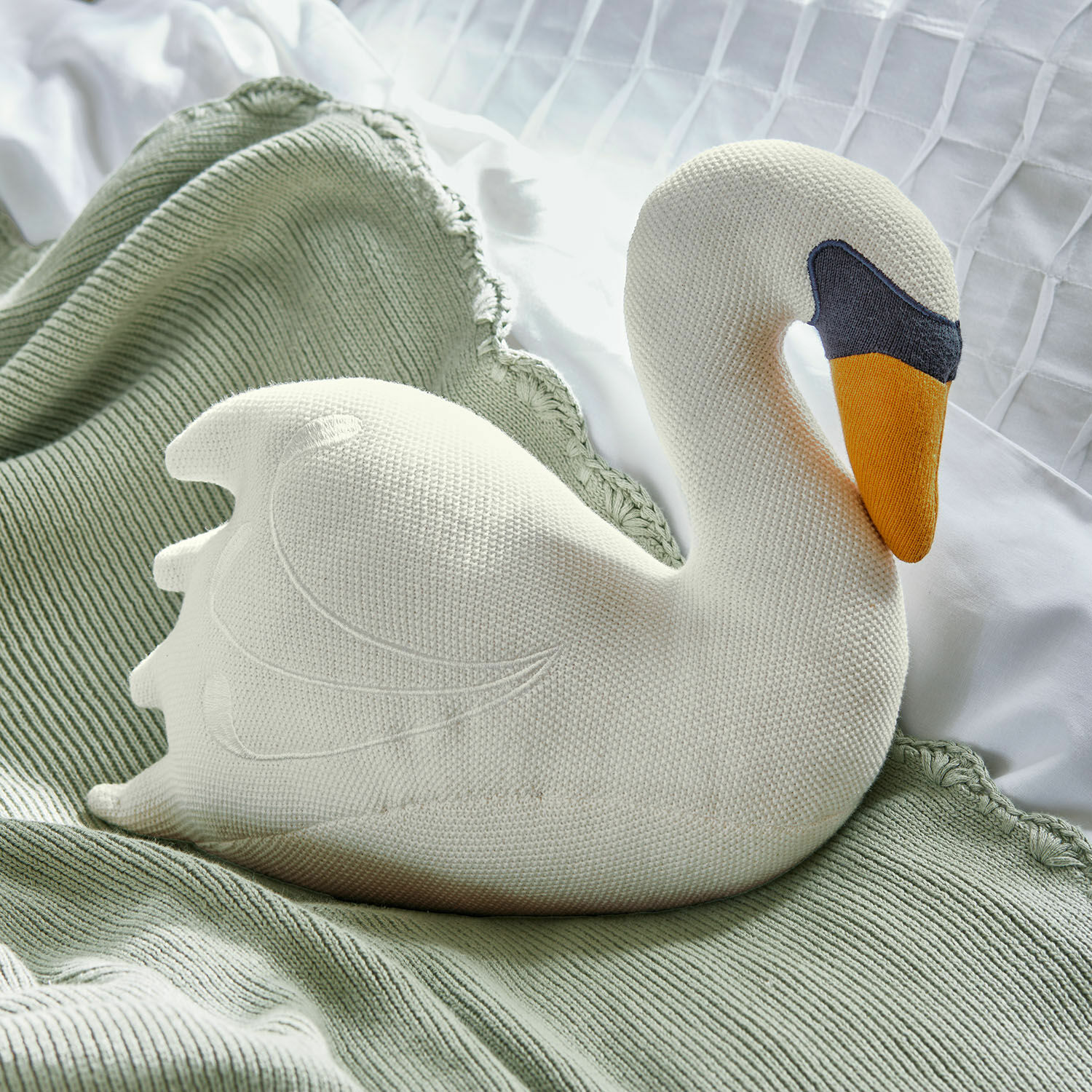 Peluche Cariella Cojín blanco en forma de cisne tejido sobre manta verde, decoración para dormitorio