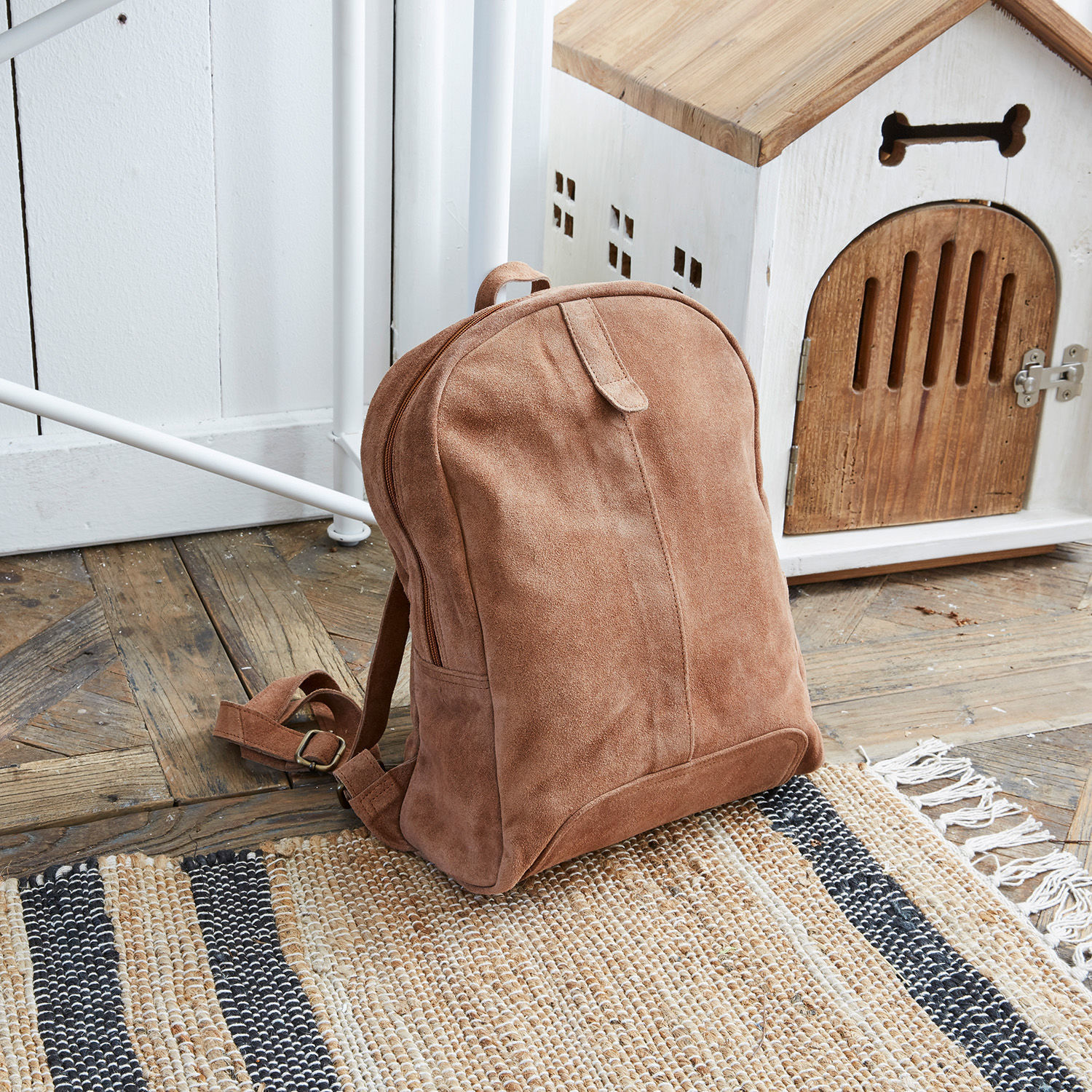Mochila Palau Mochila de ante marrón sobre suelo de madera junto a caseta blanca de madera para perros